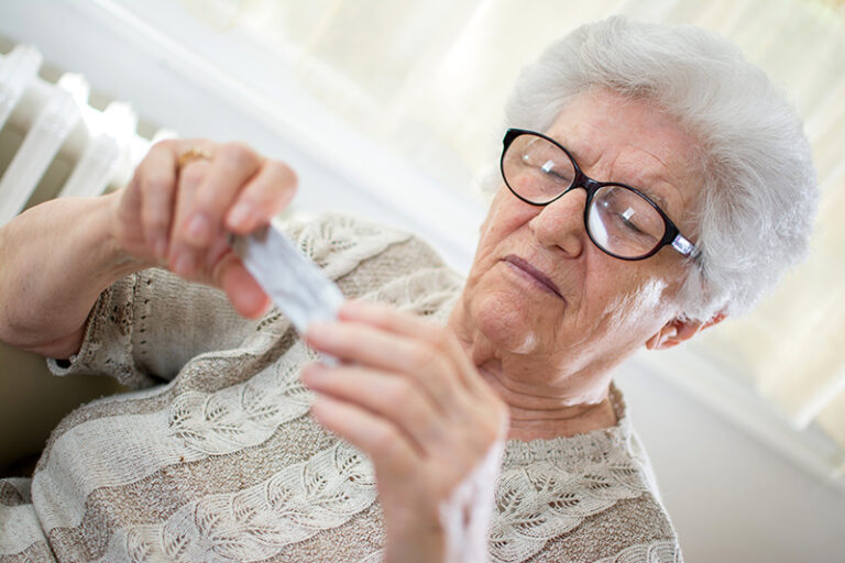 Close-up portrait of senior woman with glasses reading pill package