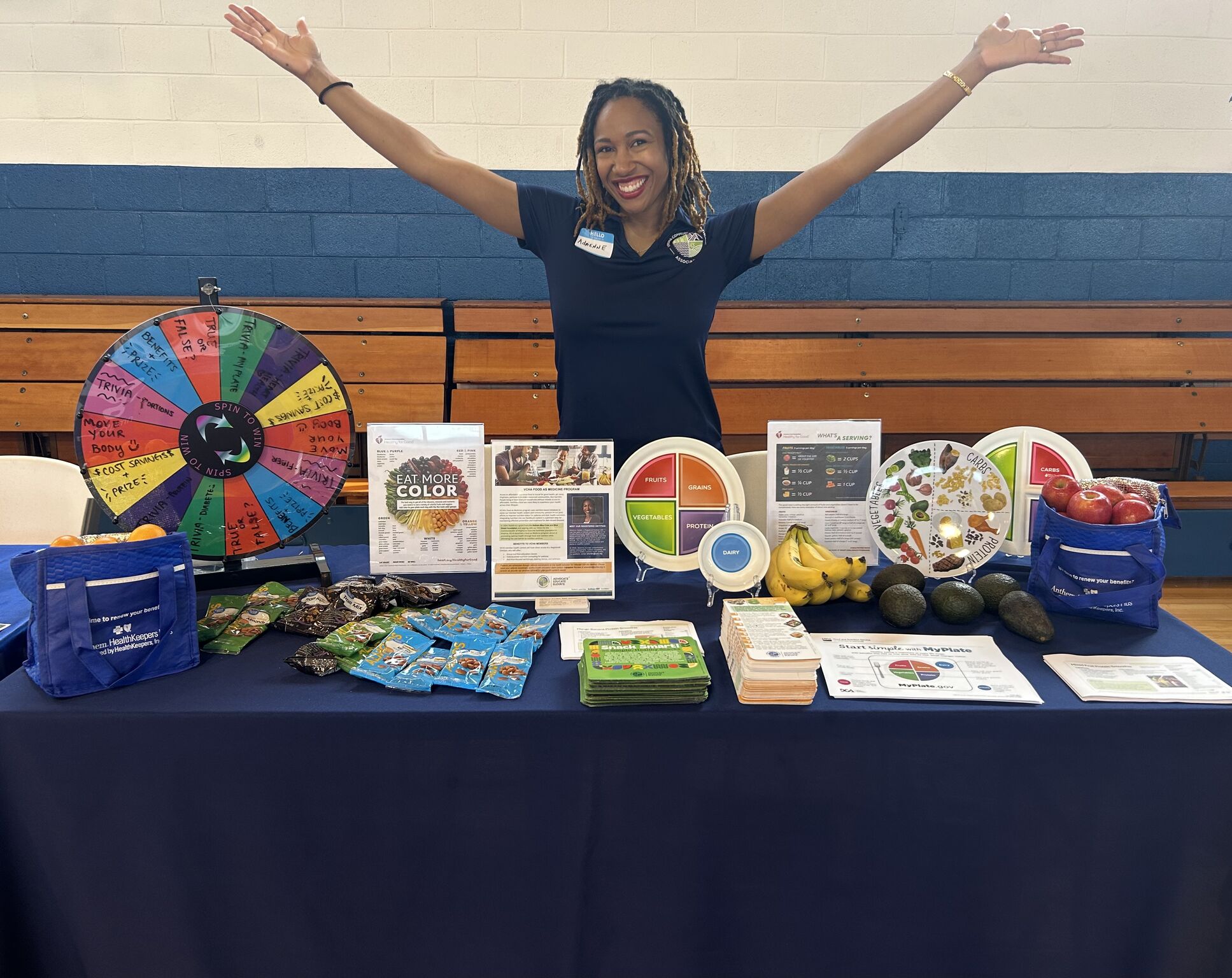 Adrienne holds her arms up proudly behind a table covered in nutrition information, snacks, and fruit