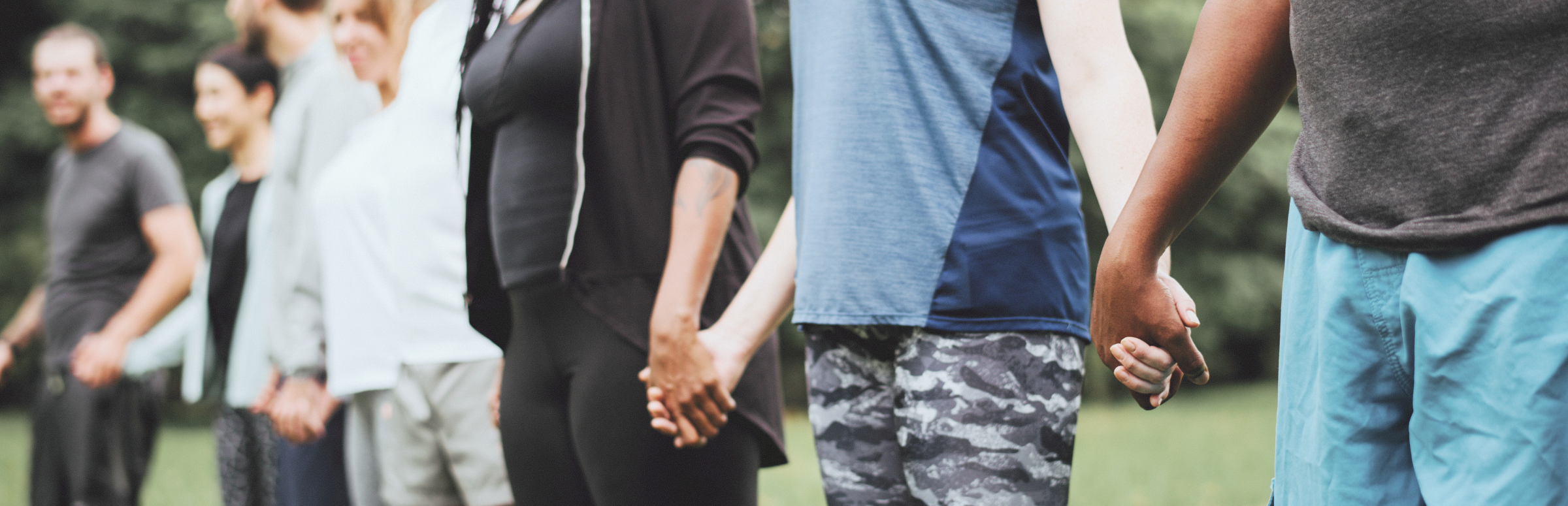 A row of people of different races and genders holding hands.