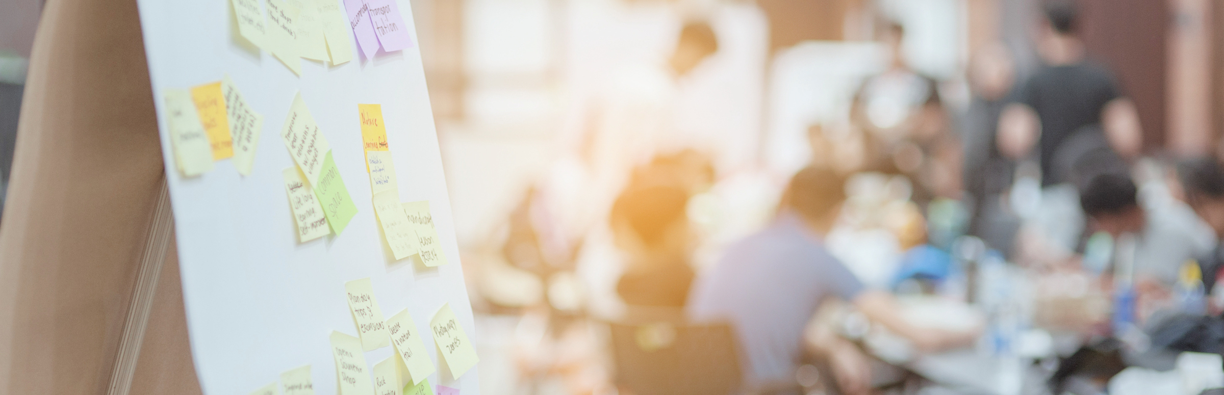 Easel covered in sticky notes with a group of people at work in the background