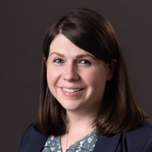 Headshot of Caitlin Longan smiling, a white woman with shoulder-length brown hair.