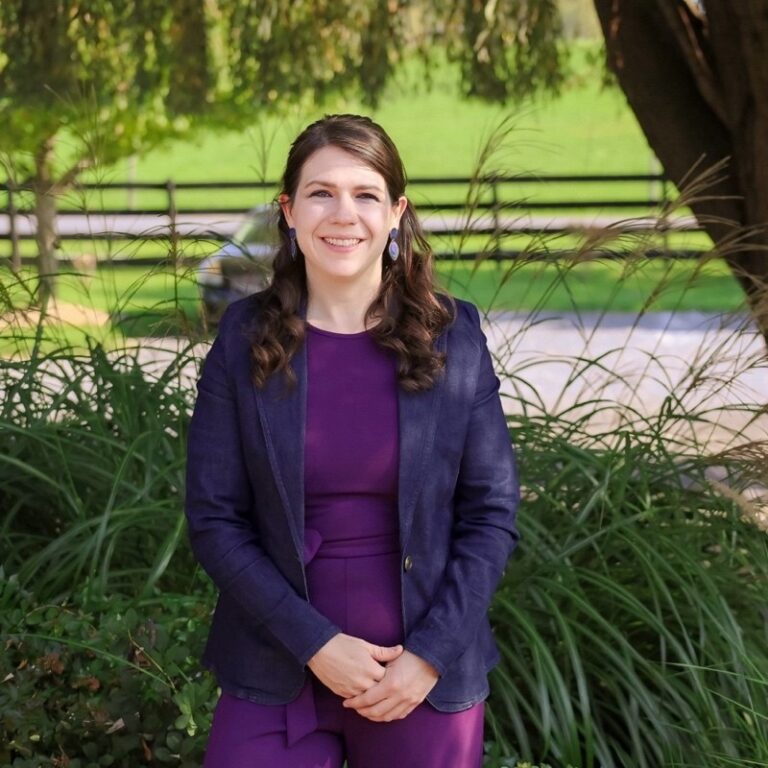 Caitlin Longan, a white woman, stands outside smiling.