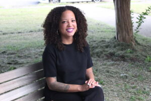 Amanda, a Black woman, sits smiling on a park bench