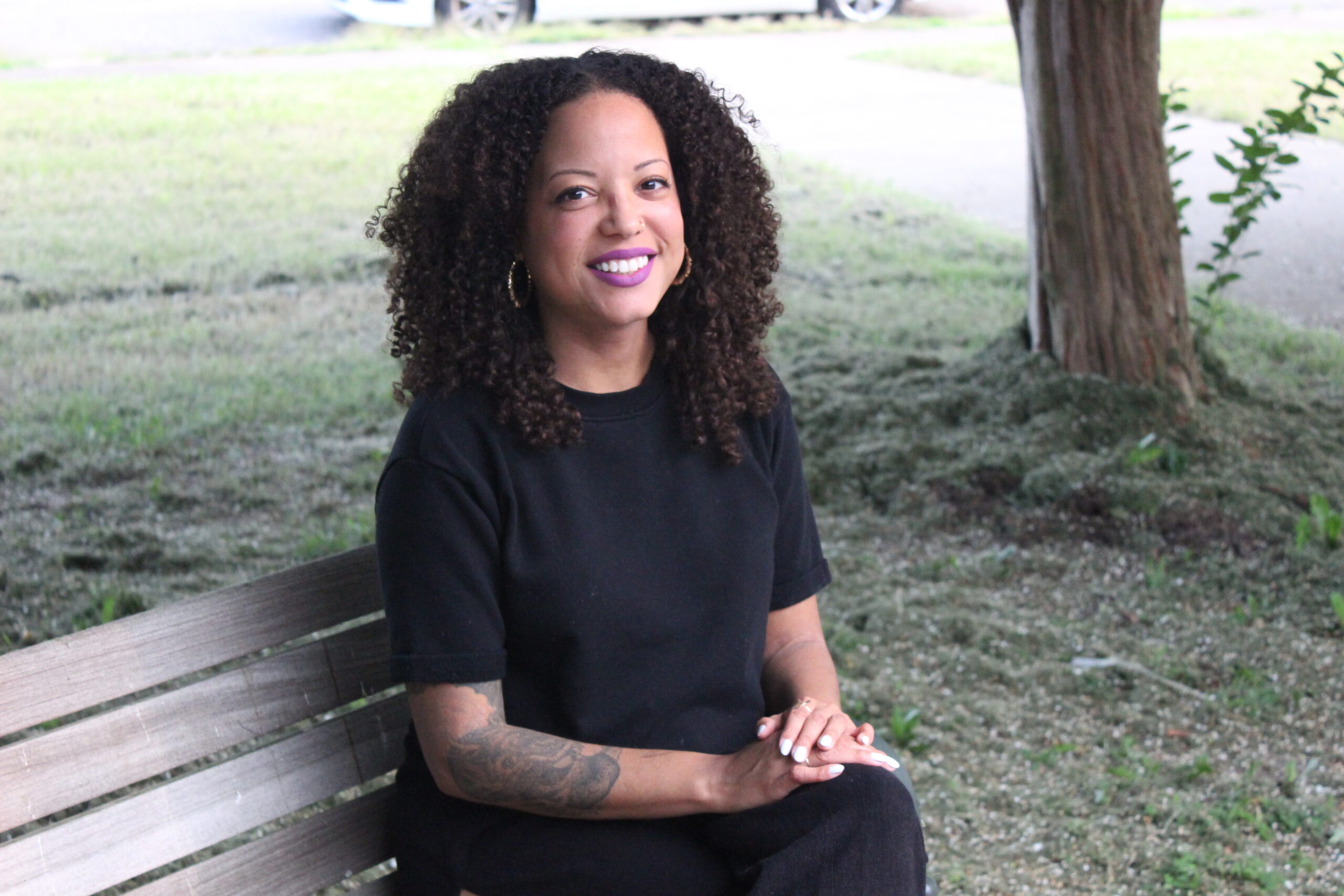 Amanda, a Black woman, sits smiling on a park bench
