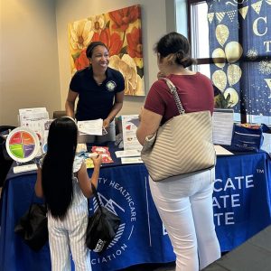 Adrienne speaks to a woman and young girl from behind a table covered in nutrition information