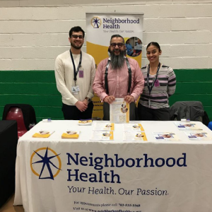 Neighborhood Health Booth with 3 people standing by the table